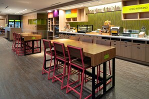 A modern breakfast area with a wooden table and red chairs, a counter with food items, and a 'Good Morning' sign.