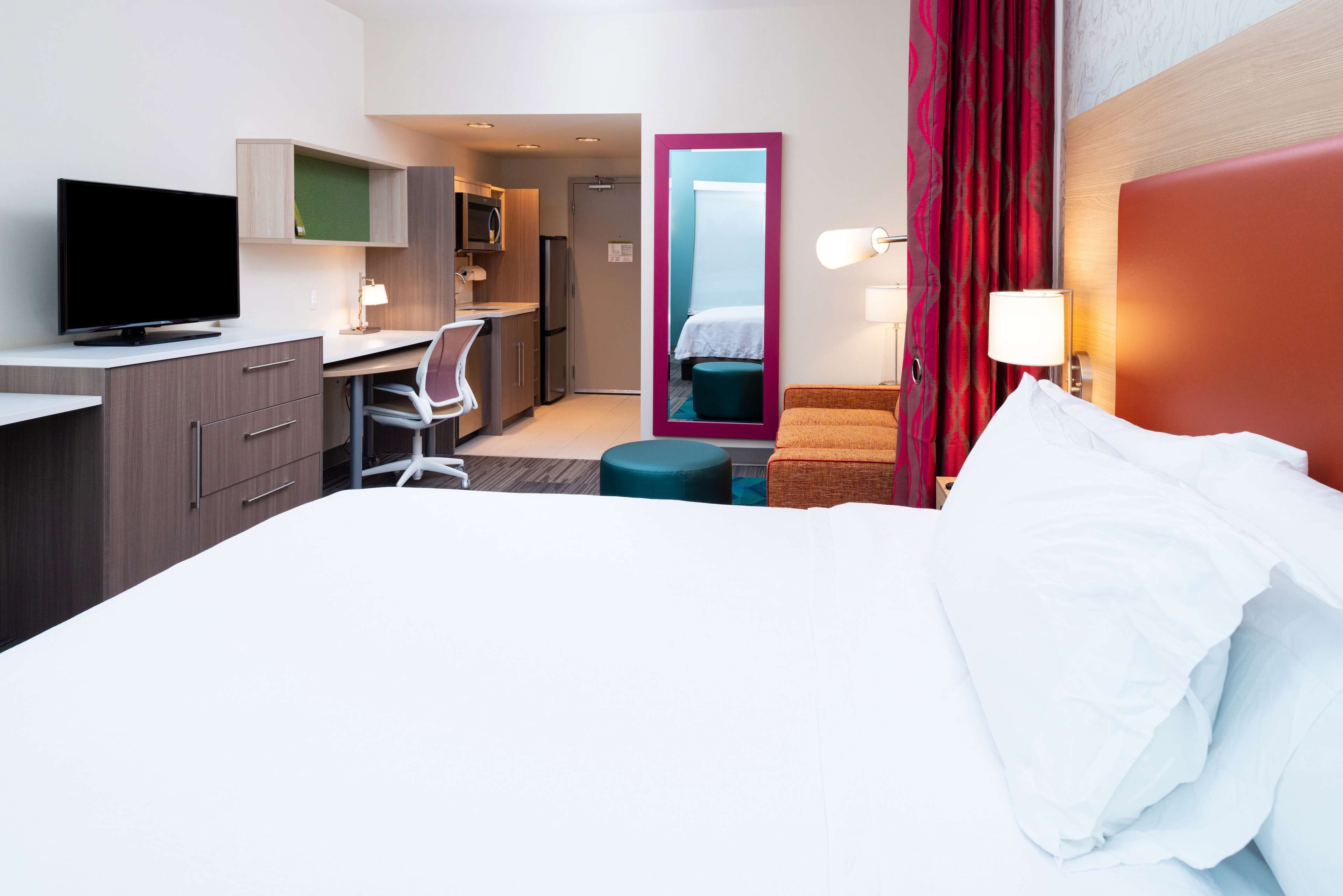 Une chambre d’hôtel comprenant un lit, un bureau avec une chaise, une télévision, un miroir et une kitchenette.