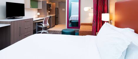 Une chambre d’hôtel comprenant un lit, un bureau avec une chaise, une télévision, un miroir et une kitchenette.