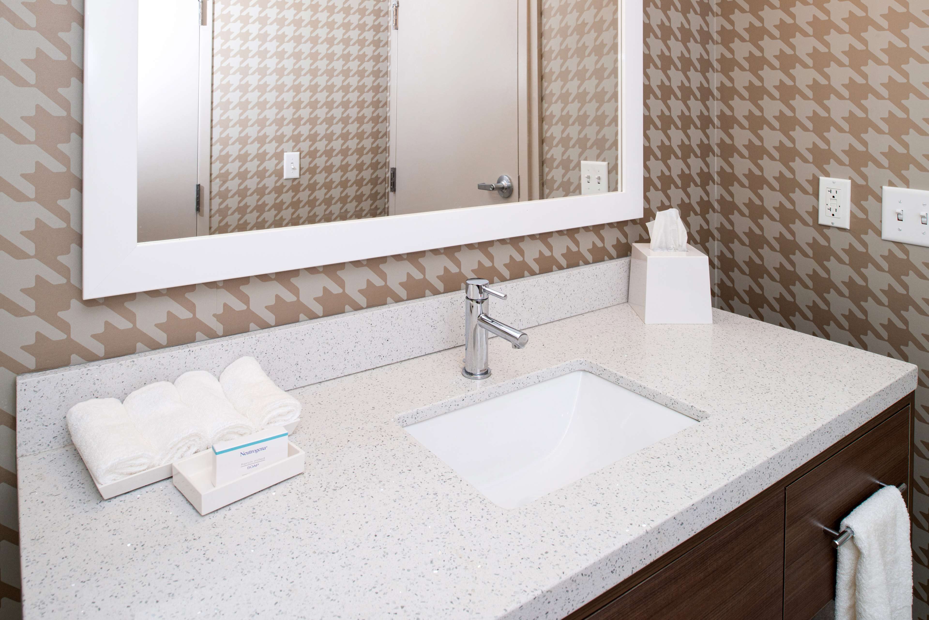A hotel bathroom with a large mirror, white sink, and towel rack.