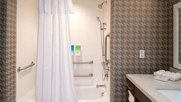 A bathroom with a bathtub, shower, and handrails. There are towels on the counter and a mirror.