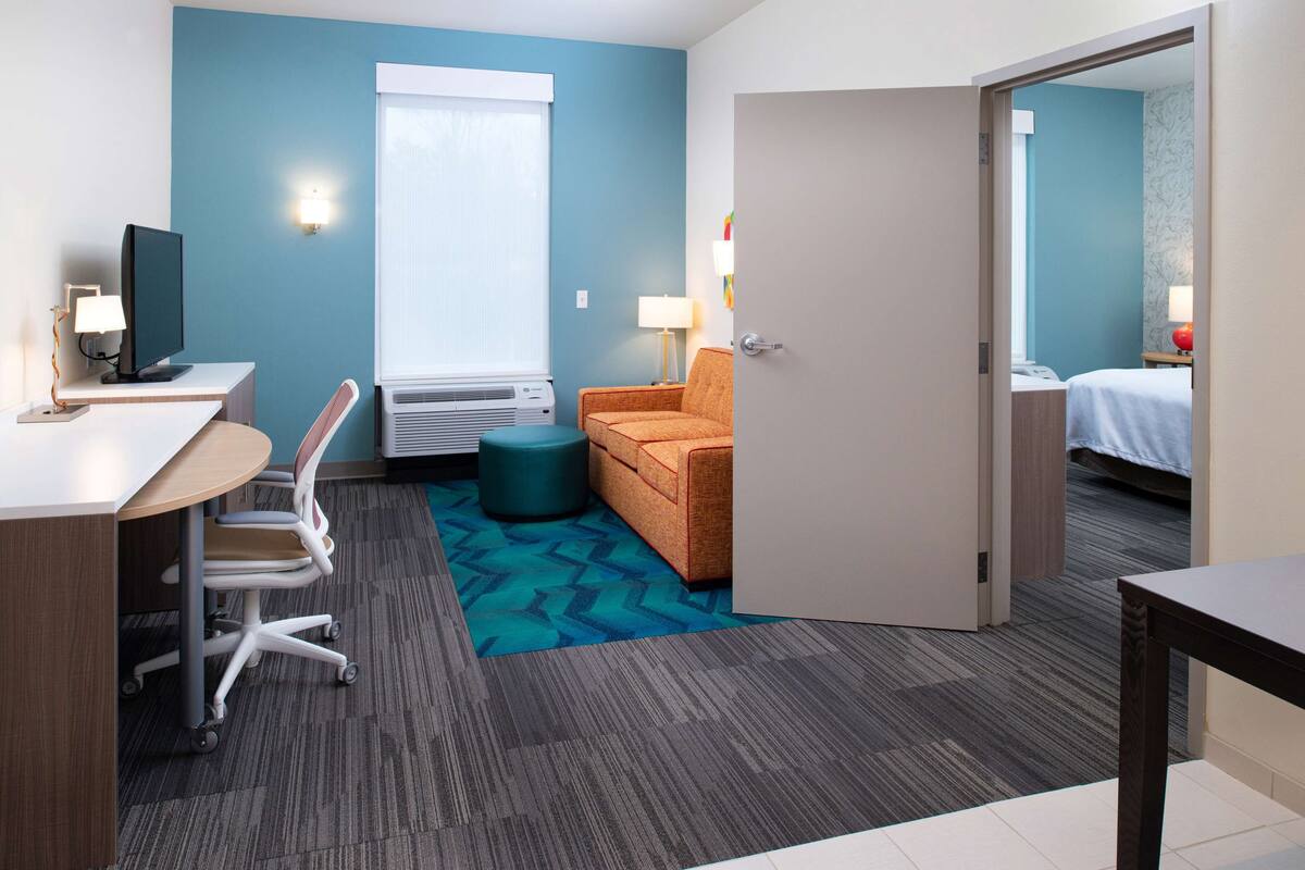 A hotel room with a desk, chair, and a small orange sofa.
