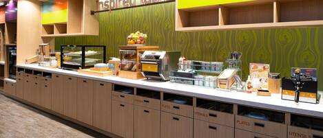 A breakfast buffet area with labeled sections for plates, utensils, and a coffee station.