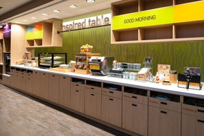 Un espace buffet pour le petit-déjeuner, avec des zones clairement identifiées pour les assiettes, les couverts et un coin café.