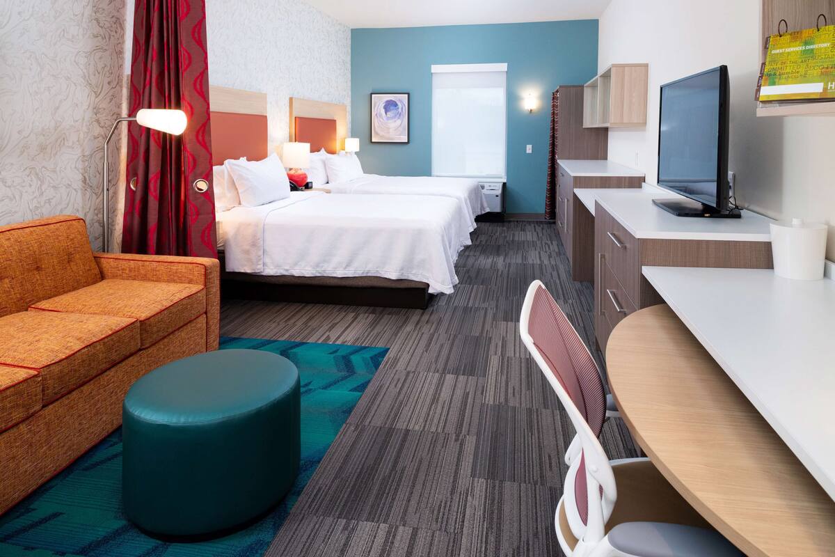 A hotel room with a bed, a desk, a chair, a sofa, and a television.