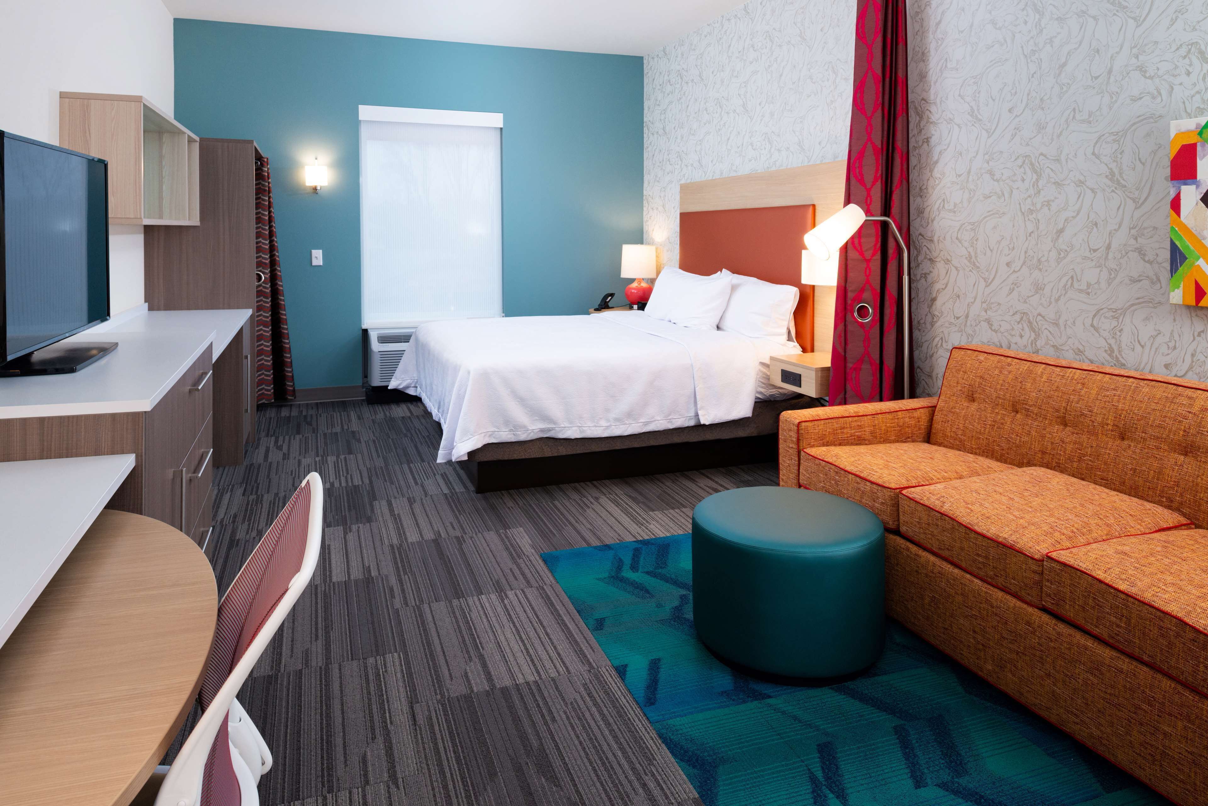 A hotel room with a bed, a desk, a sofa, and a TV.