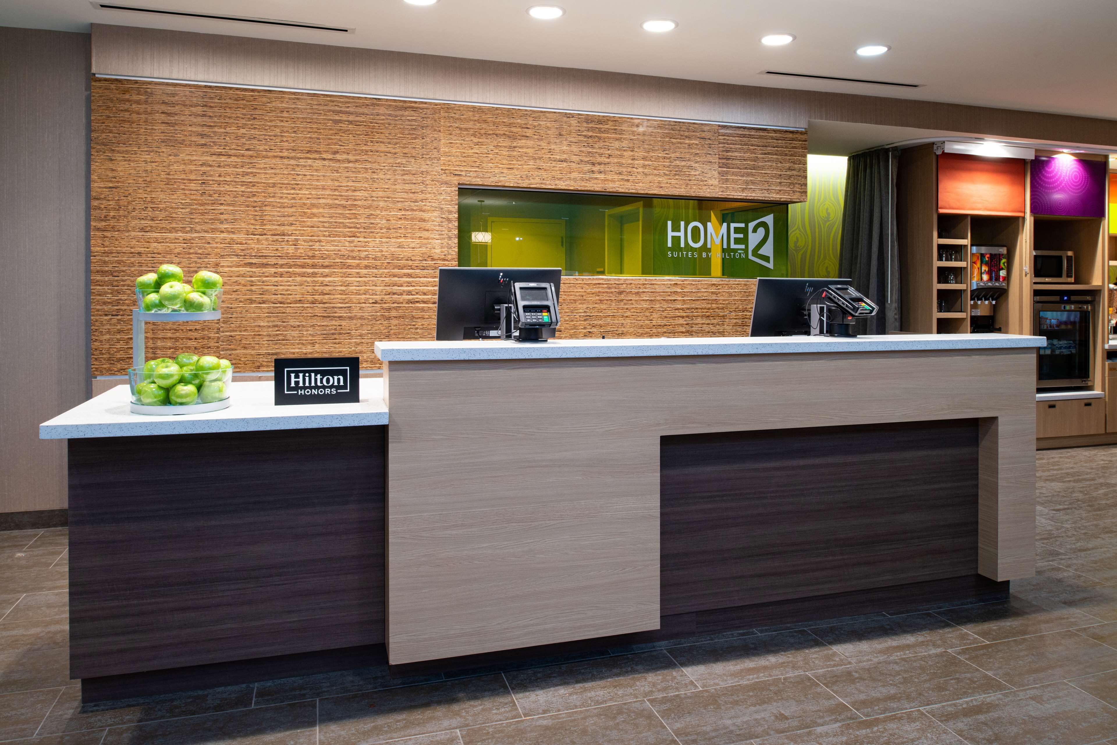A hotel reception desk with a modern design, a digital screen, and a sign indicating 'HOME2 Suites by Hilton'.