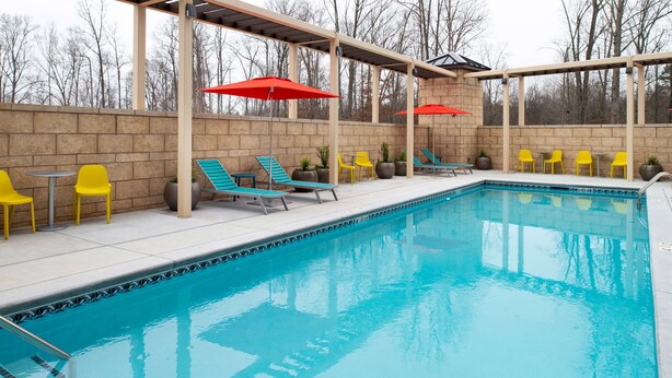 Une piscine entourée de chaises longues et de parasols, le tout bordé d’un mur de briques et avec des arbres en arrière-plan.