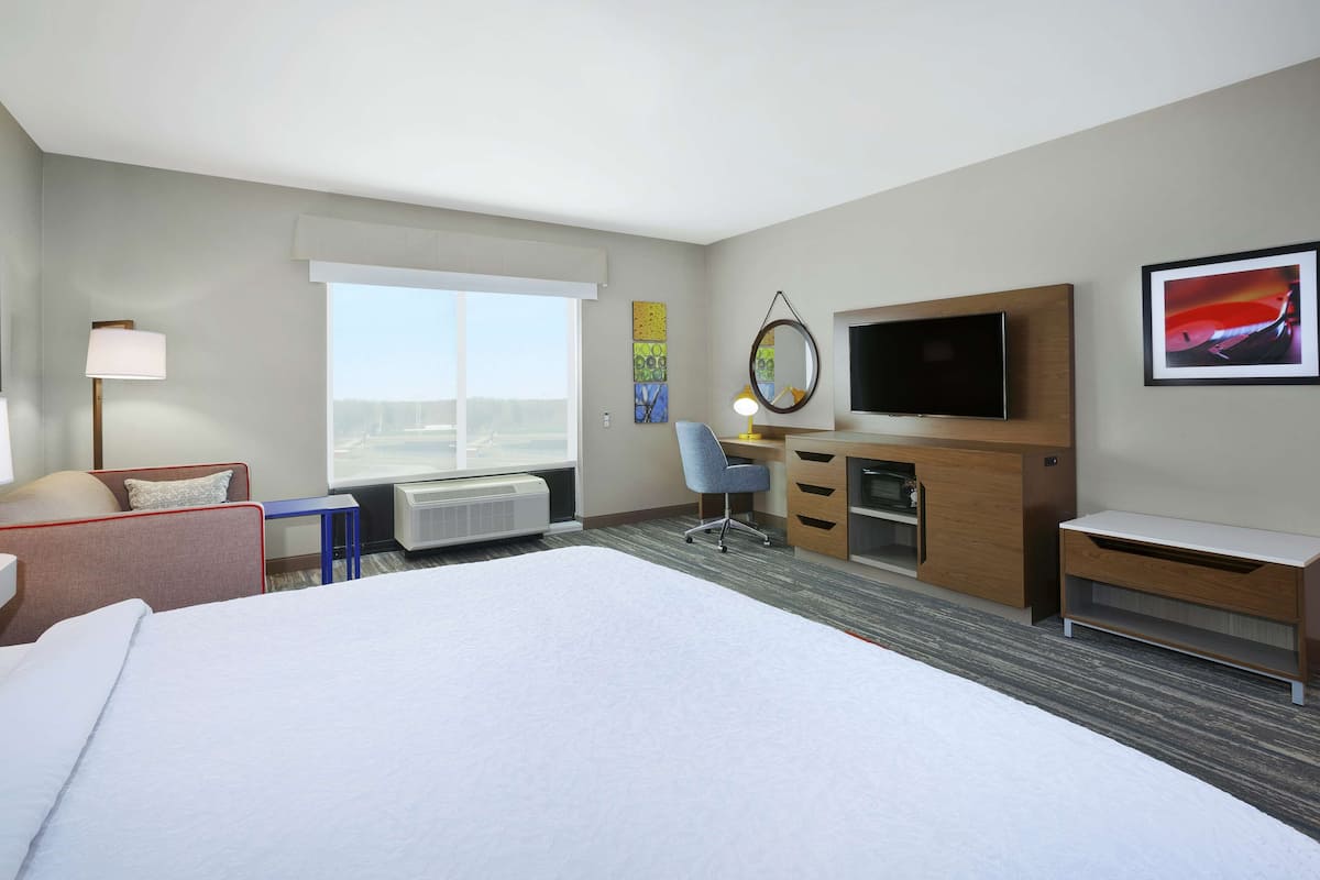 Una habitación de hotel con una cama grande, un escritorio con una silla, un televisor y una ventana con vistas.