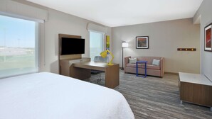 A hotel room with a large bed, a desk with a chair, a TV, a sofa, and a window with a view of the outside. - Hampton Inn & Suites Grandville Grand Rapids South (Grandville)