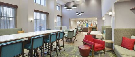 A modern dining area with high tables, chairs, and a mix of red and green seating.