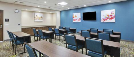 A conference room with multiple tables and chairs, a clock, and two paintings on the wall.