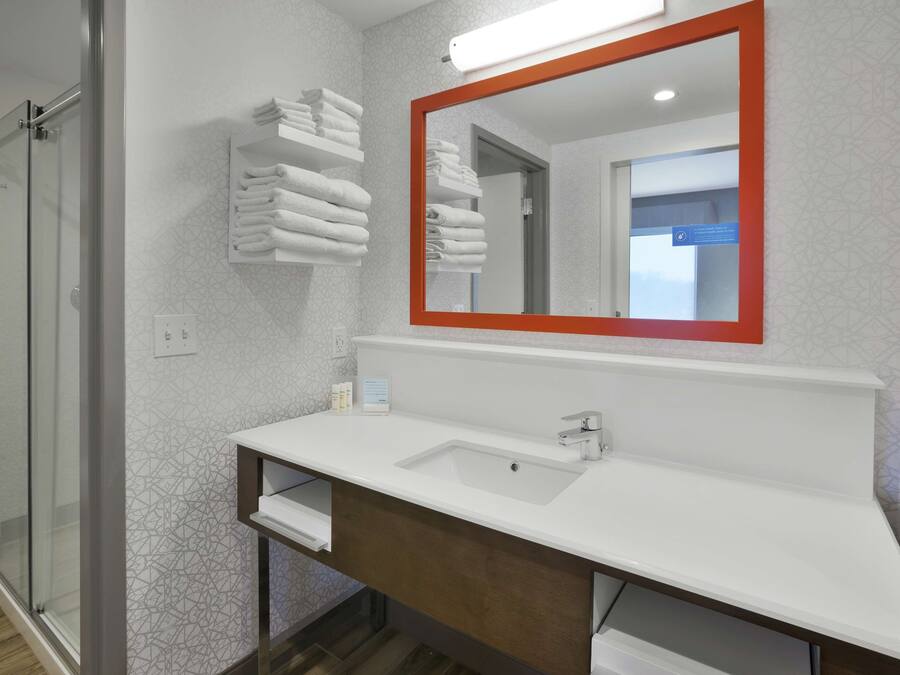 A modern bathroom with a white sink, a mirror with a red frame, and a towel rack with neatly folded towels.