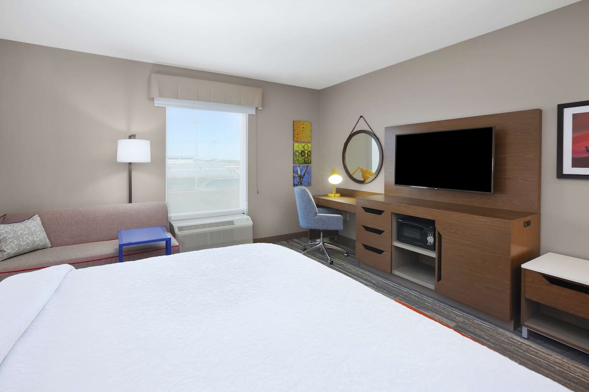 Habitación de hotel con una cama grande, un escritorio con computadora, televisión, sofá y ventana con vista.