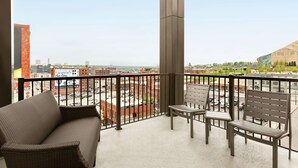 Een balkon met een rieten bank en twee stoelen, met uitzicht op een stadsgezicht met gebouwen en een heldere lucht.