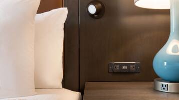 A neatly made bed with white pillows, a bedside lamp, and a control panel with two USB ports.