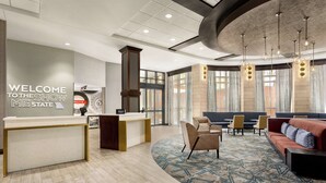 Een hotellobby met een receptiebalie, een zithoek en grote ramen.