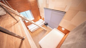 Une pièce avec un plancher en bois, un lit avec une literie blanche, une petite table et une fenêtre.