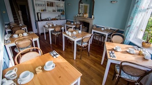 A dining area with multiple wooden tables and wicker chairs, equipped with tea sets and dining utensils. - Harbour Heights Guest House (Torquay)