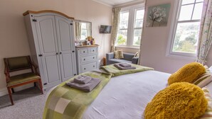 A bedroom with a bed, a wardrobe, a chair, a television, and a window with curtains. - Harbour Heights Guest House (Torquay)