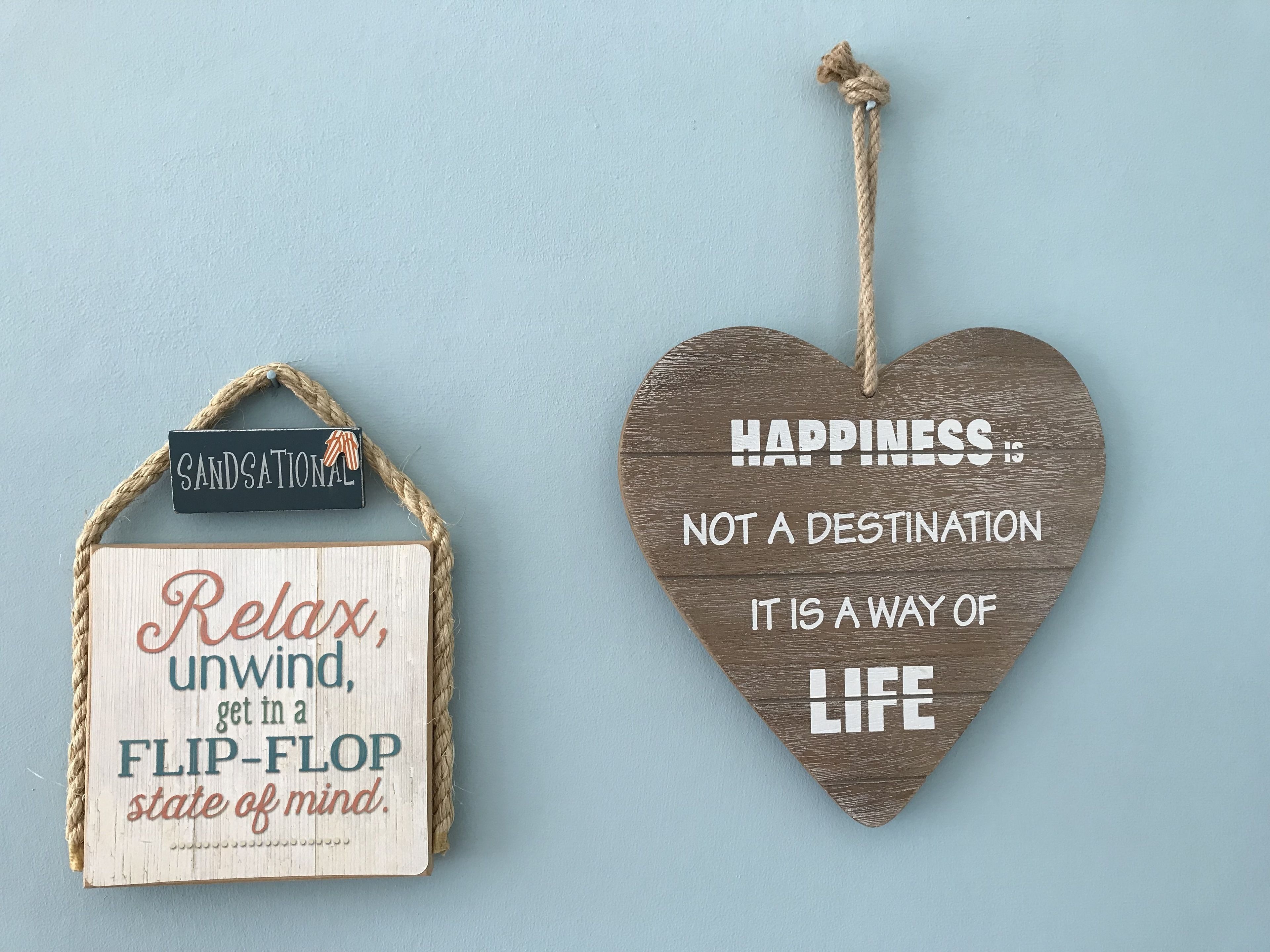 Two wooden signs with motivational quotes, one rectangular and one heart-shaped, hanging on a light blue wall.