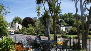 An outdoor patio with a table and chairs, surrounded by plants and a view of the city. - Harbour Heights Guest House (Torquay)