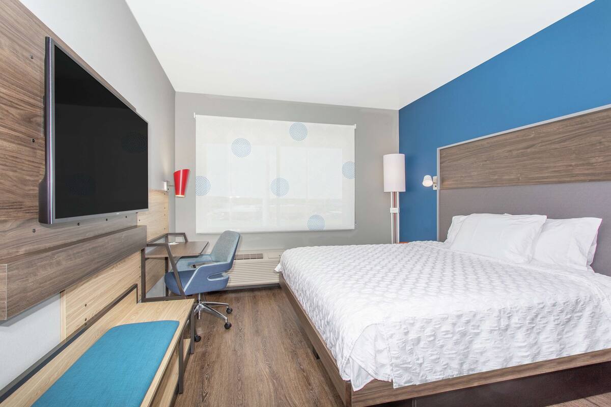A hotel room with a bed, a desk with a chair, a television, and a window with a curtain.