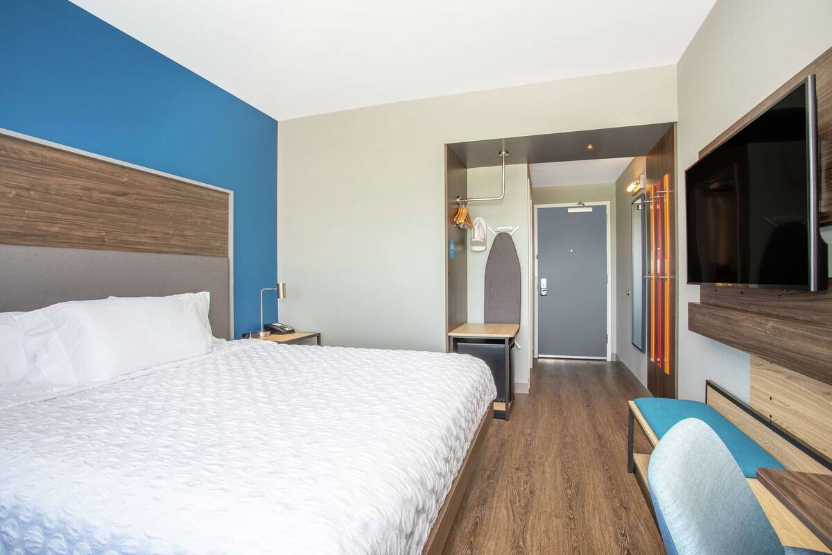 A modern hotel room with a large bed, a TV, a bench, and a walk-in closet.