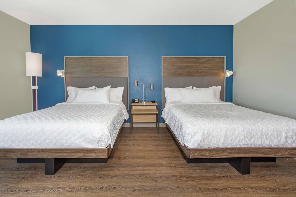 A hotel room with two beds, a nightstand, and a lamp.