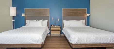 A hotel room with two beds, a nightstand, and a lamp.