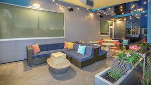 An outdoor seating area with a sofa, chairs, and a table, surrounded by potted plants and string lights. - Tru by Hilton Salt Lake City Midvale (Midvale)