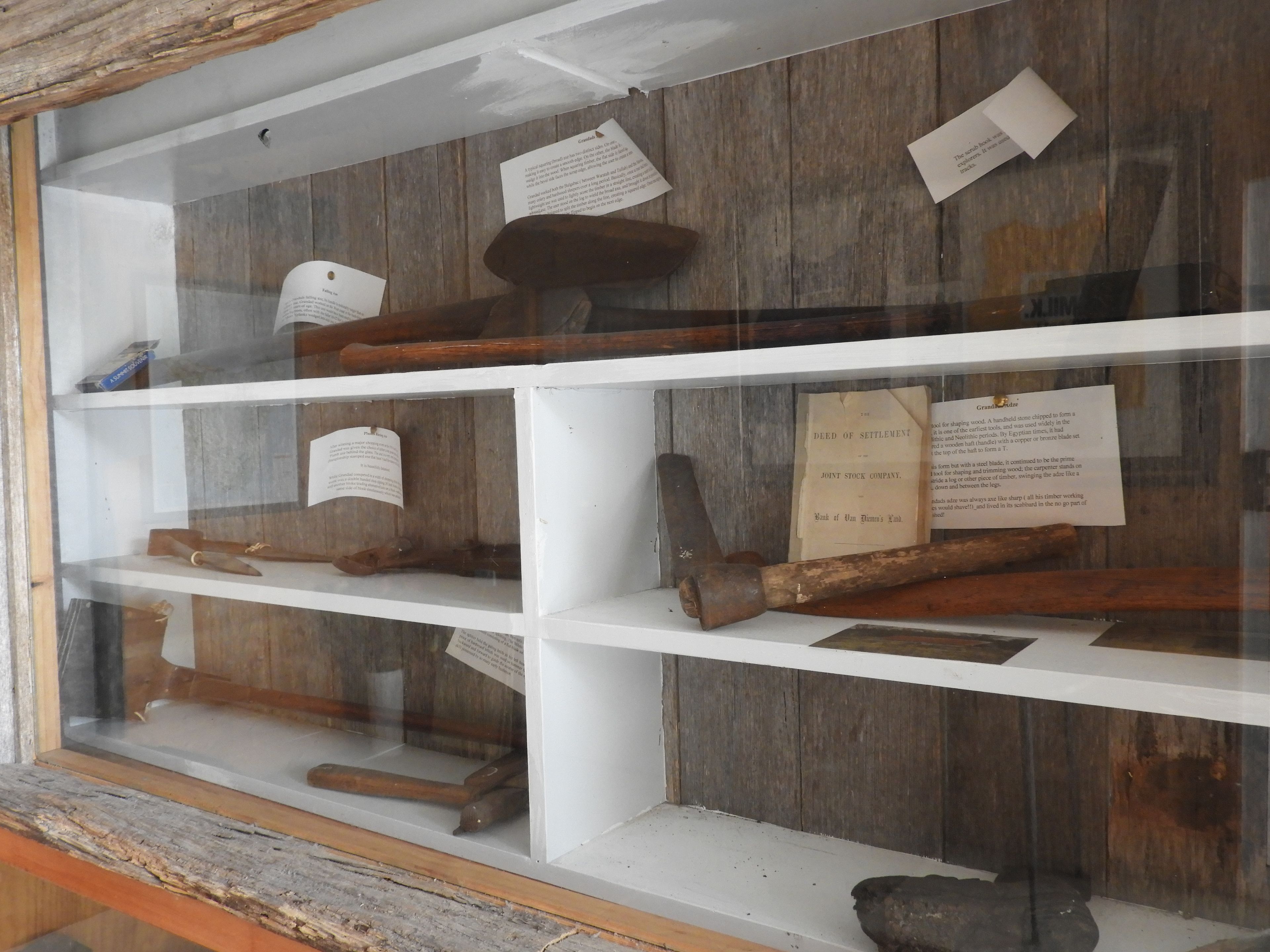 Una vitrina con artefactos de madera y documentos, incluyendo un 'Deed of Settlement' y un 'hacha de abuelo'.