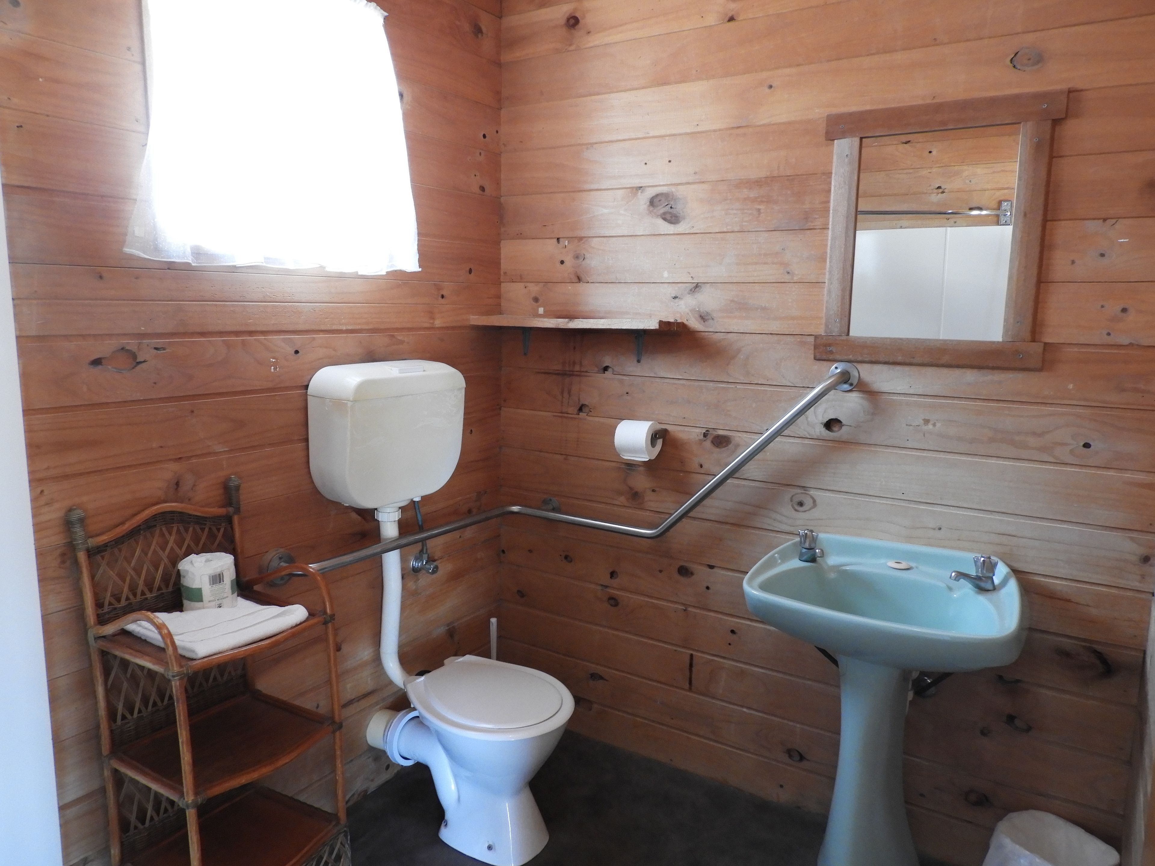 Un baño con paneles de madera, un inodoro, un lavamanos, una silla de madera y un espejo.