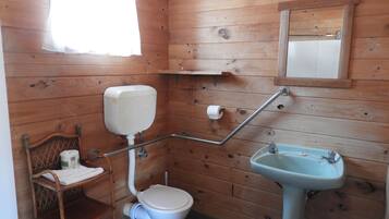 Un baño con paneles de madera, un inodoro, un lavamanos, una silla de madera y un espejo.