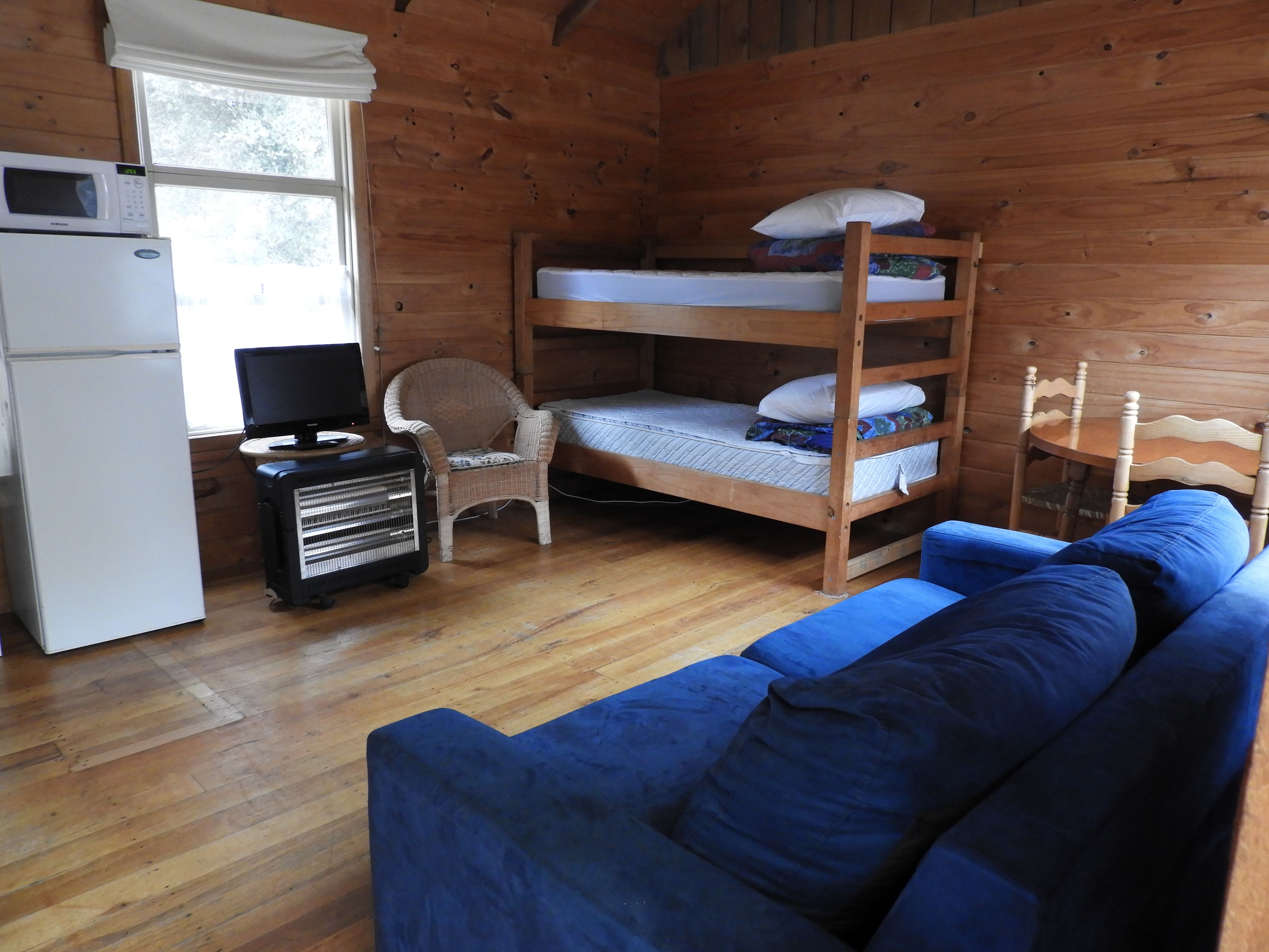 A cabin with a bunk bed, a white refrigerator, a television, a wicker chair, and a blue sofa.