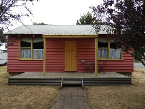 A small, single-story house with a red exterior and a yellow door. There is a small porch with a table and two chairs. - Somerset Caravan Park (Somerset)