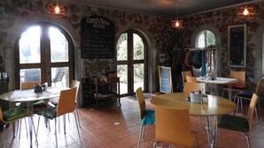 Un restaurante con paredes de piedra, ventanas de arco y un cartel con la carta. Mesas y sillas dispuestas para comer.