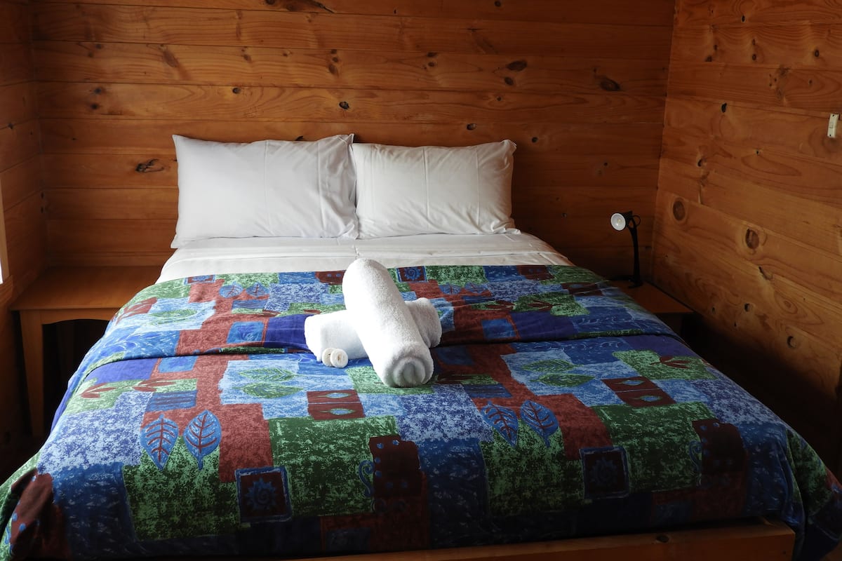 A wooden cabin room with a bed, white pillows, and a colorful quilt.