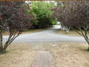 A paved pathway leading to a road flanked by trees with red leaves. - Somerset Caravan Park (Somerset)