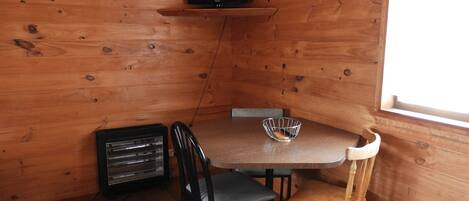 A wooden cabin interior with a TV on a shelf, a table with chairs, and a window.