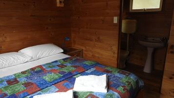 Een houten kamer met een bed, een nachtkastje, een raam en een badkamer met een wastafel en toilet.