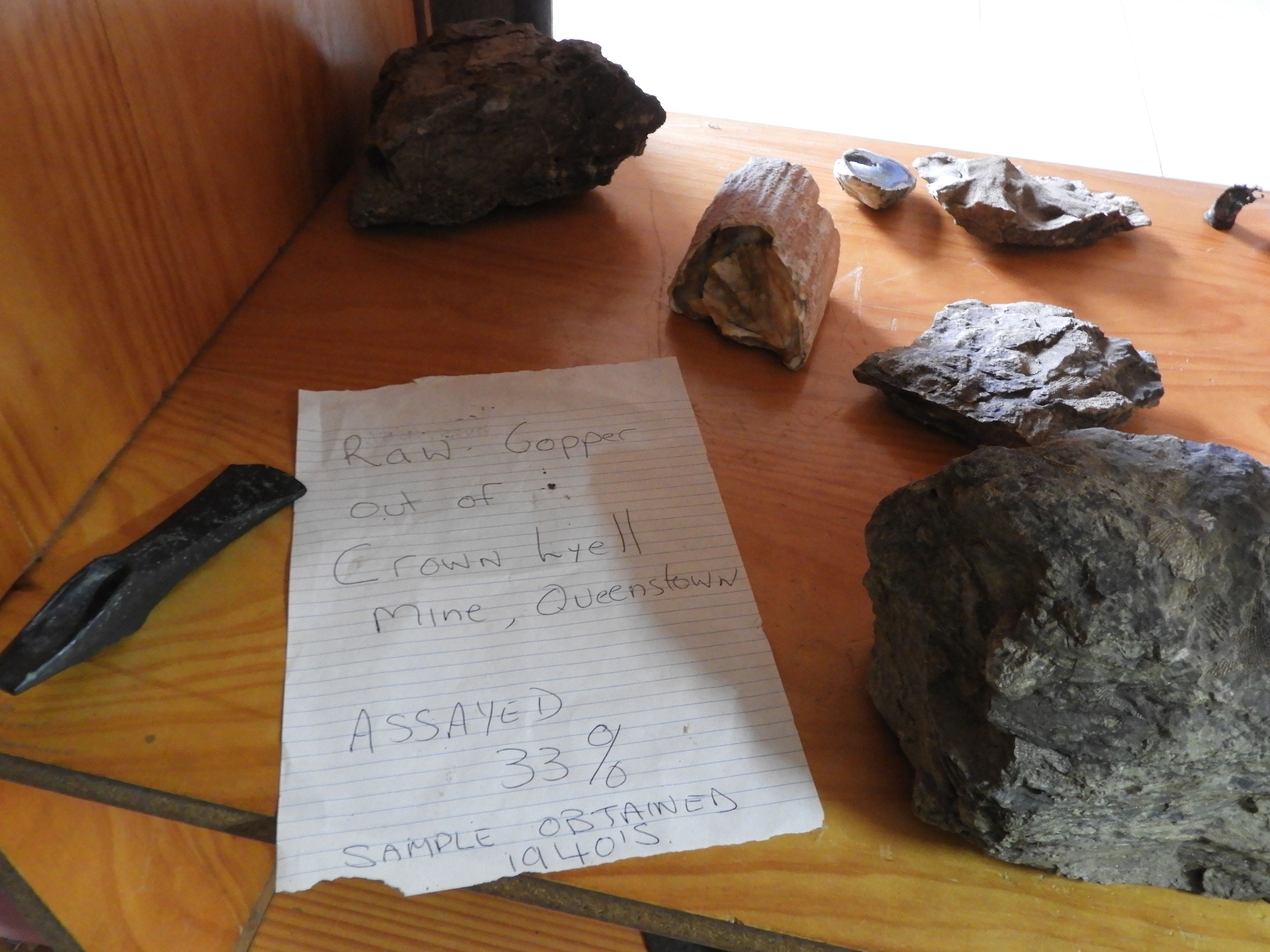 A handwritten note on a piece of paper with text and a list of rocks on a wooden surface.