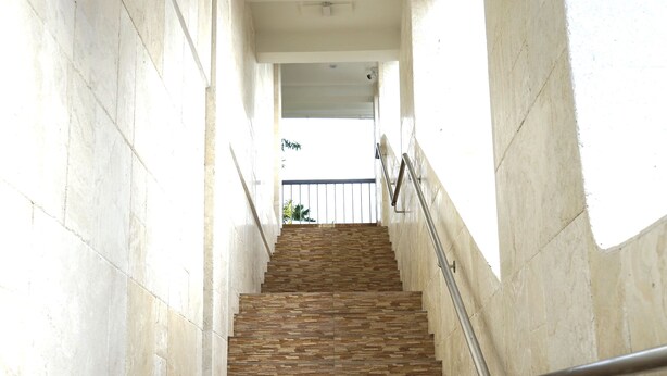 Eine Treppe mit Steinwänden und einem Metallgeländer, die zu einem hellen Bereich oben führt.