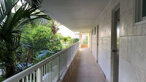 Ein Korridor mit Fliesenboden, weißen Geländern und Blick auf Grünfläche.
