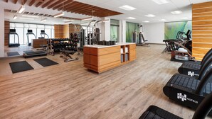 Une salle de sport équipée de tapis de course, d’appareils de musculation et d’un comptoir d’accueil en bois.