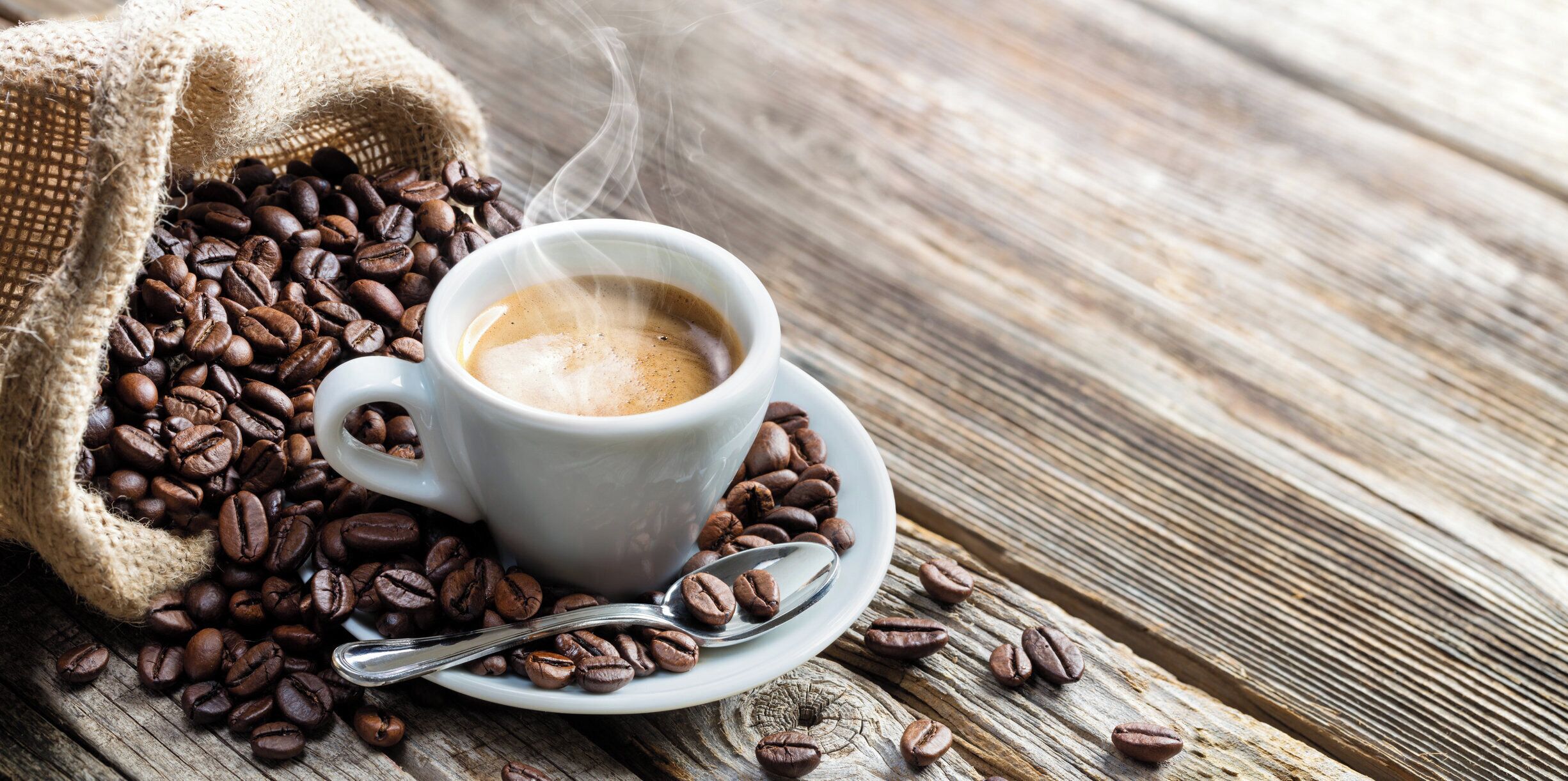 Een kop koffie met damp, omringd door koffiebonen op een ruw houten oppervlak.