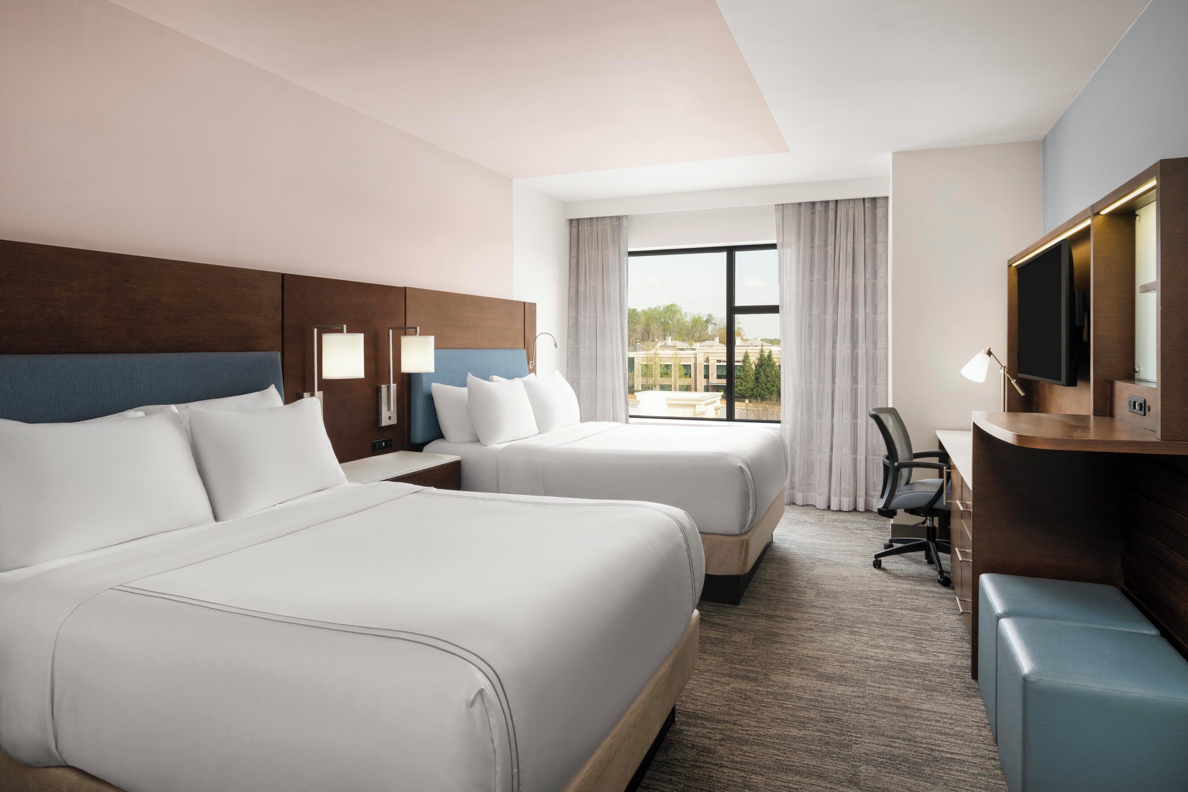 Une chambre d’hôtel avec deux lits, un bureau, une chaise, une télévision et une fenêtre avec des rideaux.