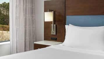 Habitación de hotel con cama, mesita de noche, lámpara de pared y ventana con cortinas.