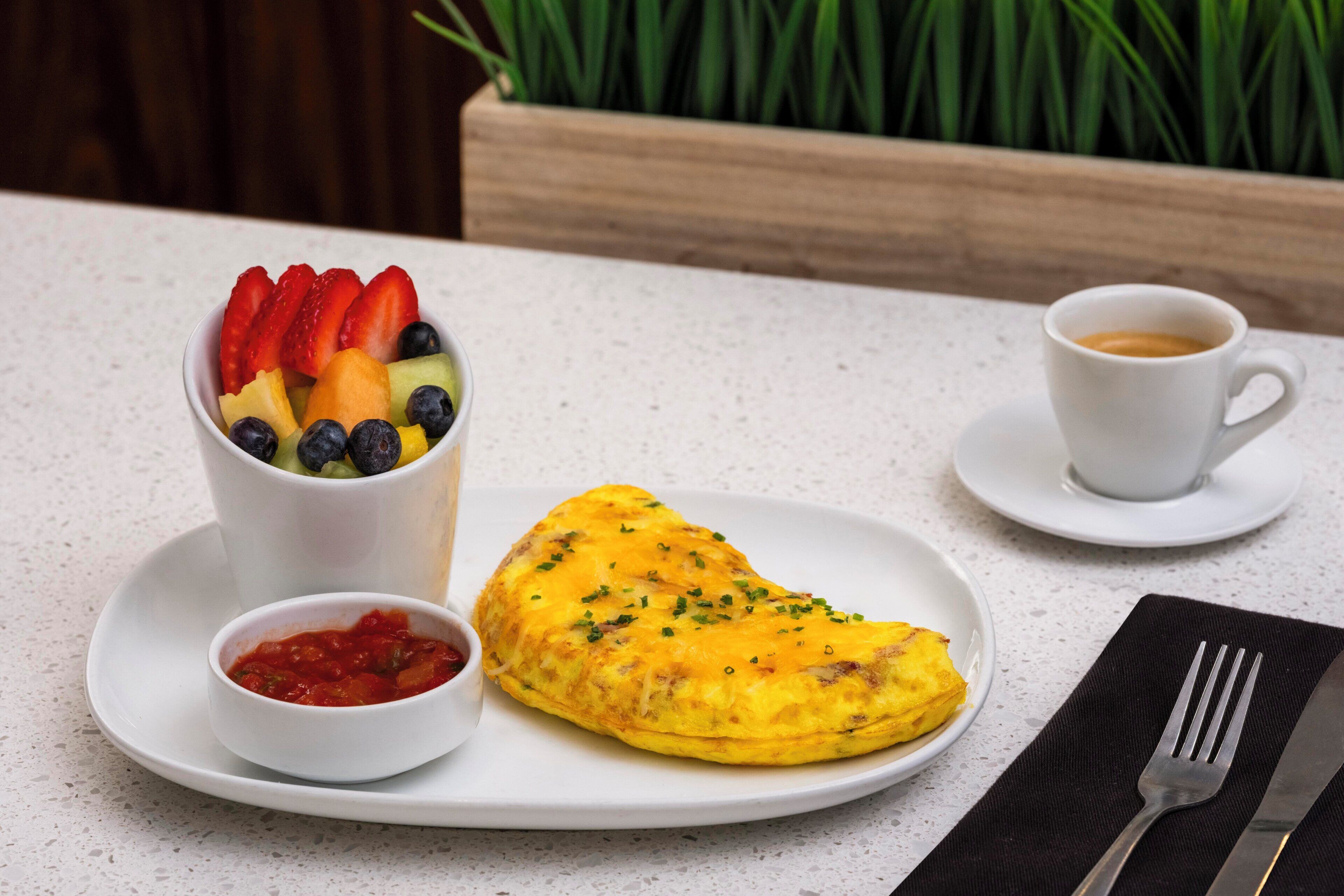 A breakfast setting with a plate of food, a cup of coffee, and a bowl of fruit salad.