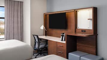 A hotel room with a bed, a desk with a chair, a TV, a coffee maker, and a window with curtains.